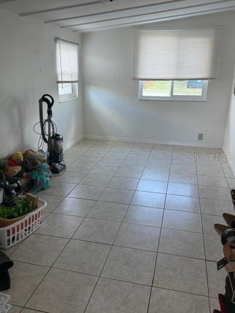 unfurnished room featuring a wealth of natural light, beamed ceiling, and light tile patterned floors