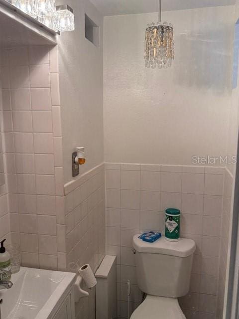 bathroom featuring a chandelier, toilet, and tile walls