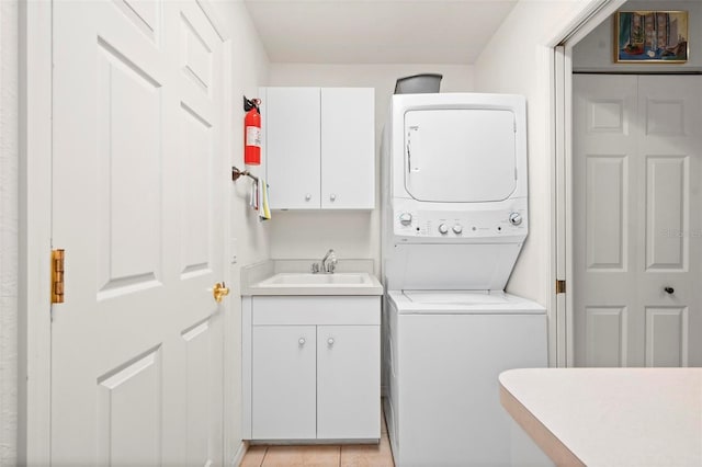 laundry area featuring cabinets, light tile patterned flooring, stacked washer and clothes dryer, and sink