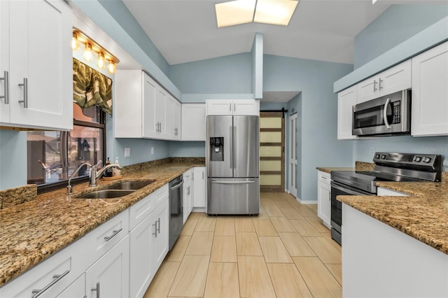 kitchen with sink, dark stone counters, lofted ceiling, white cabinets, and appliances with stainless steel finishes