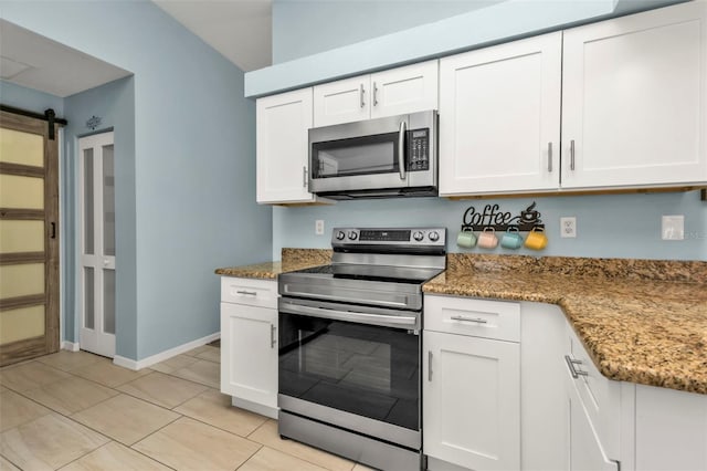 kitchen with dark stone counters, white cabinets, a barn door, light tile patterned floors, and appliances with stainless steel finishes