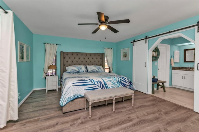 bedroom with hardwood / wood-style floors, ceiling fan, a barn door, and ensuite bath