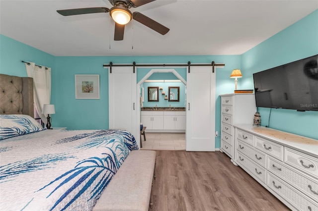 bedroom featuring ensuite bathroom, a barn door, light wood-type flooring, and ceiling fan