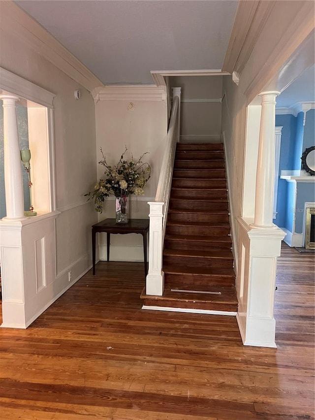 stairs with crown molding, wood-type flooring, and a fireplace