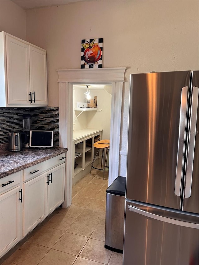 kitchen with tasteful backsplash, stainless steel refrigerator, white cabinetry, and light tile patterned flooring