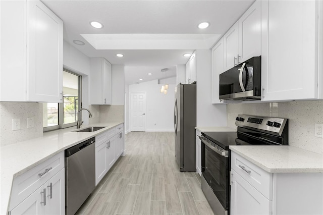 kitchen with white cabinets, appliances with stainless steel finishes, light stone counters, and sink