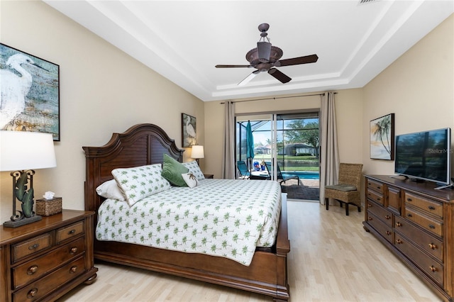 bedroom with access to outside, a raised ceiling, ceiling fan, and light wood-type flooring