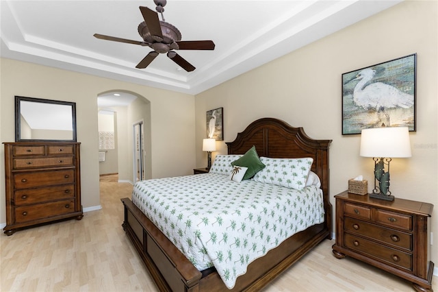 bedroom featuring a closet, light hardwood / wood-style floors, a raised ceiling, and ceiling fan