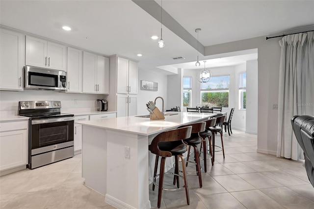 kitchen with appliances with stainless steel finishes, white cabinetry, a kitchen island with sink, and sink