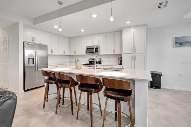 kitchen featuring appliances with stainless steel finishes, a kitchen island with sink, pendant lighting, white cabinetry, and a breakfast bar area