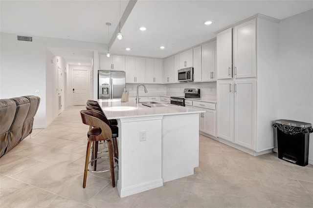 kitchen with sink, an island with sink, a breakfast bar area, white cabinets, and appliances with stainless steel finishes