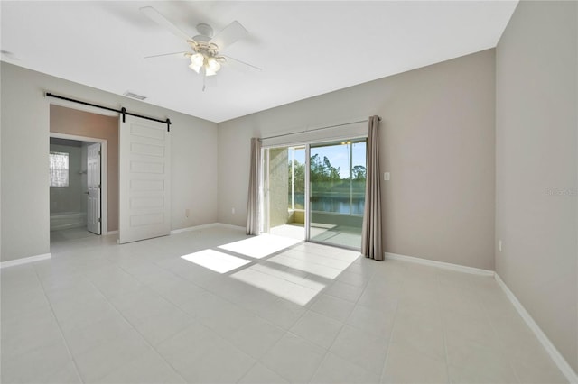 tiled empty room featuring a water view, a barn door, and ceiling fan