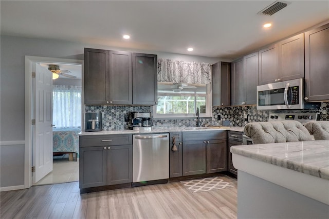 kitchen featuring light wood-type flooring, backsplash, stainless steel appliances, ceiling fan, and sink