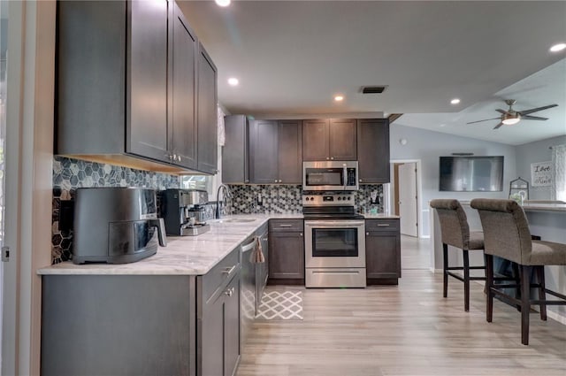 kitchen featuring appliances with stainless steel finishes, a breakfast bar, vaulted ceiling, sink, and light hardwood / wood-style flooring