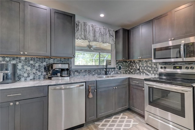 kitchen with light stone countertops, backsplash, stainless steel appliances, sink, and light hardwood / wood-style flooring