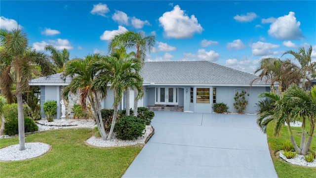 single story home featuring a front lawn, a tiled roof, concrete driveway, stucco siding, and french doors