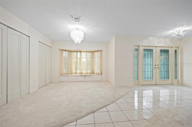 spare room featuring french doors, light colored carpet, an inviting chandelier, and a textured ceiling