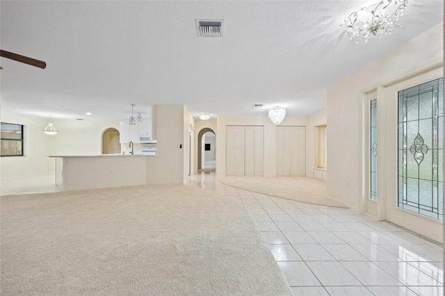 unfurnished living room featuring ceiling fan with notable chandelier, a textured ceiling, and light tile patterned floors