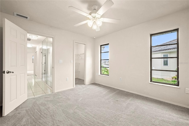 unfurnished bedroom featuring light carpet, a closet, ceiling fan, and a walk in closet