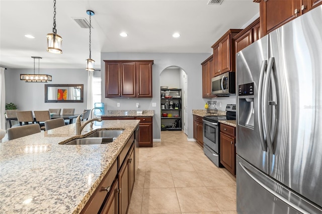 kitchen featuring sink, a breakfast bar, appliances with stainless steel finishes, light stone countertops, and decorative light fixtures