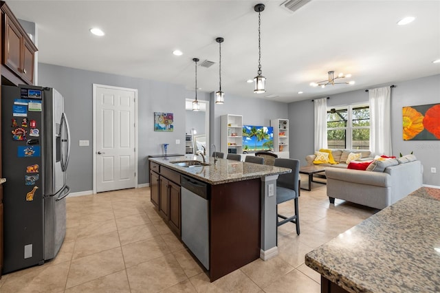 kitchen featuring decorative light fixtures, sink, a kitchen island with sink, light stone counters, and stainless steel appliances