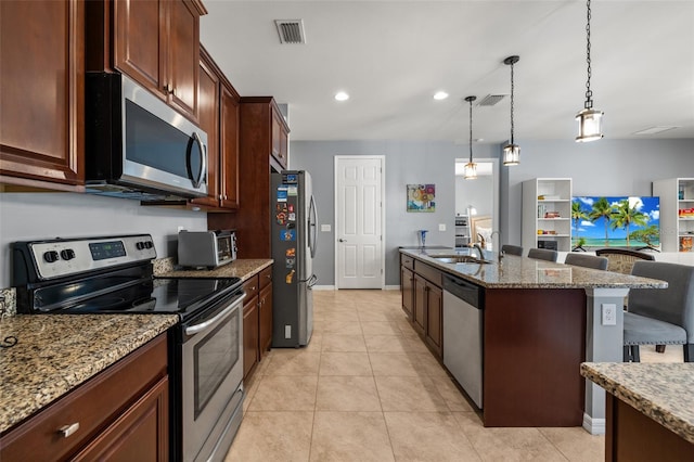 kitchen with sink, appliances with stainless steel finishes, a kitchen island with sink, a kitchen bar, and decorative light fixtures