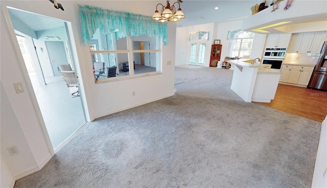 kitchen featuring light wood-type flooring, white double oven, a kitchen island with sink, decorative light fixtures, and white cabinetry