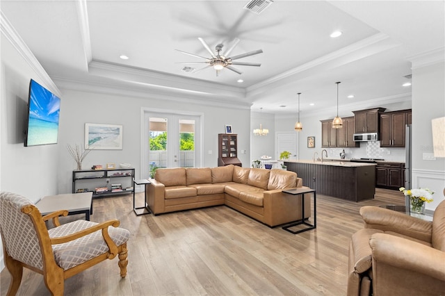 living room featuring a tray ceiling, ceiling fan with notable chandelier, ornamental molding, and light hardwood / wood-style flooring