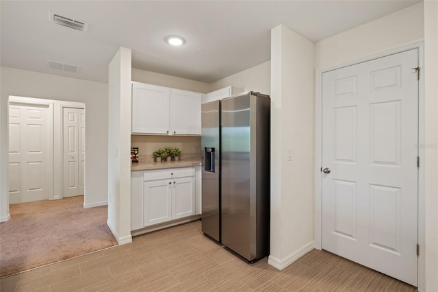 kitchen with light carpet, stainless steel refrigerator with ice dispenser, and white cabinetry