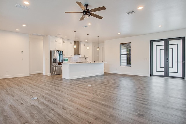 unfurnished living room featuring ceiling fan, sink, french doors, and light wood-type flooring