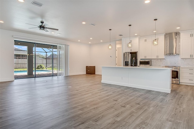 kitchen featuring pendant lighting, an island with sink, stainless steel appliances, and wall chimney range hood