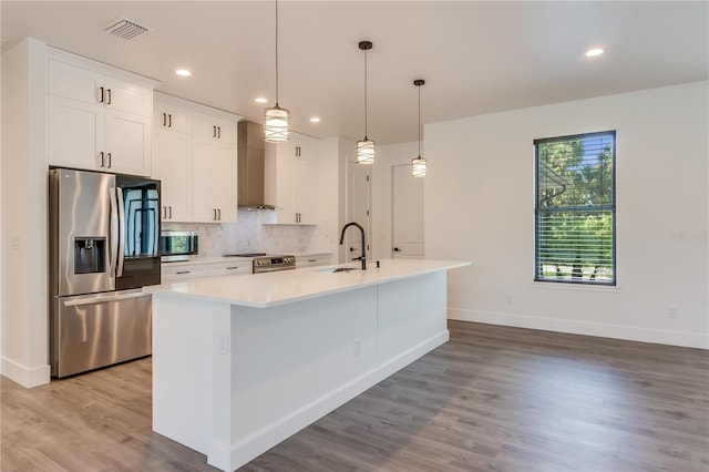 kitchen with wall chimney exhaust hood, an island with sink, light hardwood / wood-style floors, white cabinetry, and stainless steel appliances