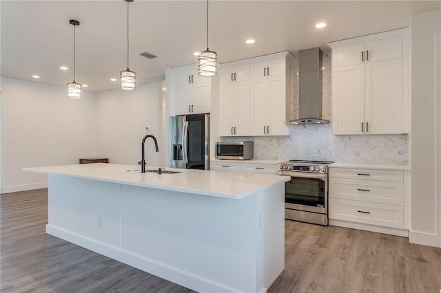 kitchen with wall chimney exhaust hood, white cabinetry, stainless steel appliances, and an island with sink