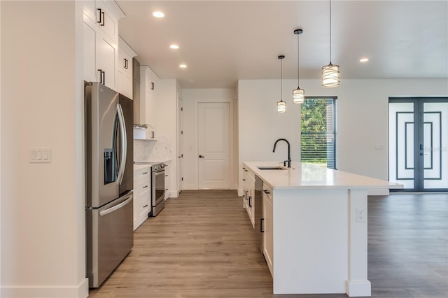 kitchen with a kitchen island with sink, white cabinets, sink, appliances with stainless steel finishes, and decorative light fixtures