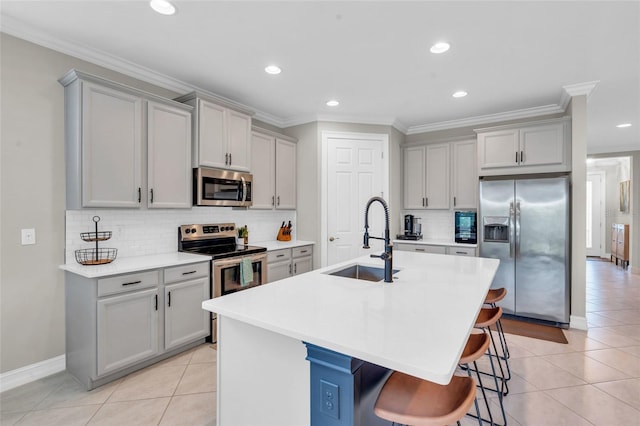 kitchen featuring a center island with sink, a kitchen breakfast bar, sink, gray cabinets, and appliances with stainless steel finishes