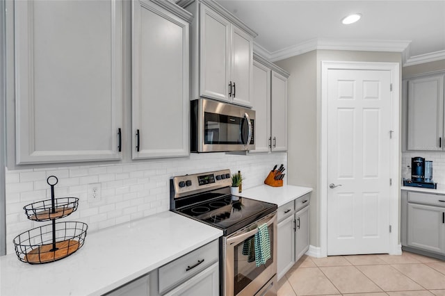 kitchen featuring gray cabinetry, backsplash, crown molding, light tile patterned floors, and appliances with stainless steel finishes