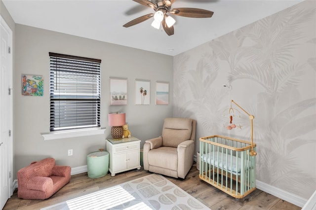 bedroom with hardwood / wood-style floors, ceiling fan, and a nursery area