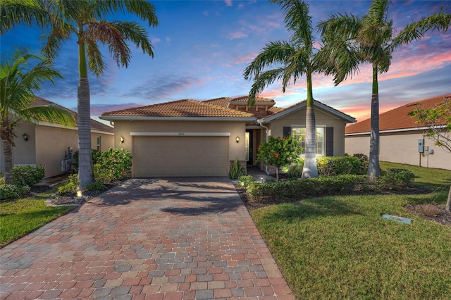 view of front of house with decorative driveway, a tile roof, a yard, stucco siding, and an attached garage