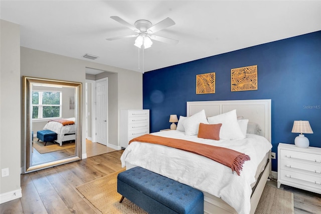 bedroom featuring visible vents, an accent wall, a ceiling fan, wood finished floors, and baseboards