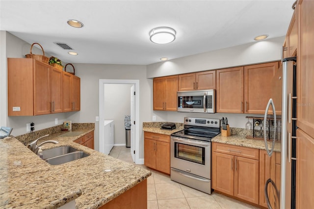 kitchen with sink, independent washer and dryer, light stone countertops, appliances with stainless steel finishes, and light tile patterned flooring