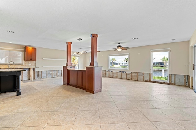 kitchen with ceiling fan, hanging light fixtures, light tile patterned floors, decorative columns, and a water view