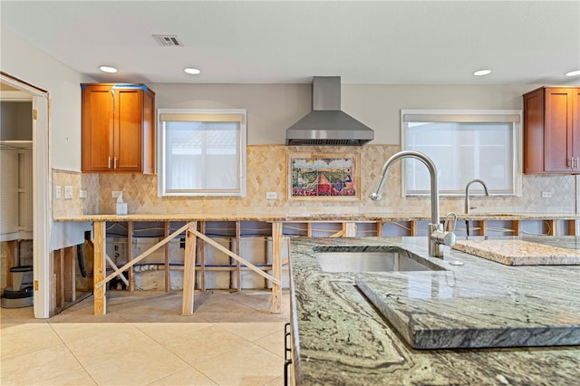 kitchen featuring light stone countertops, sink, wall chimney range hood, decorative backsplash, and light tile patterned floors