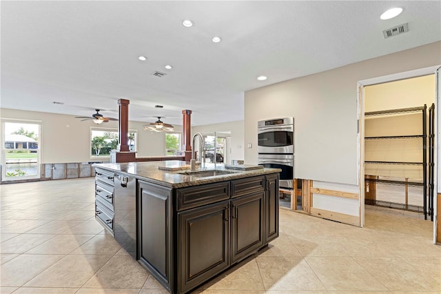 kitchen featuring sink, stainless steel double oven, dark stone countertops, a kitchen island with sink, and dark brown cabinets