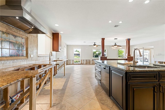 kitchen featuring light tile patterned floors, light stone counters, wall chimney exhaust hood, and sink