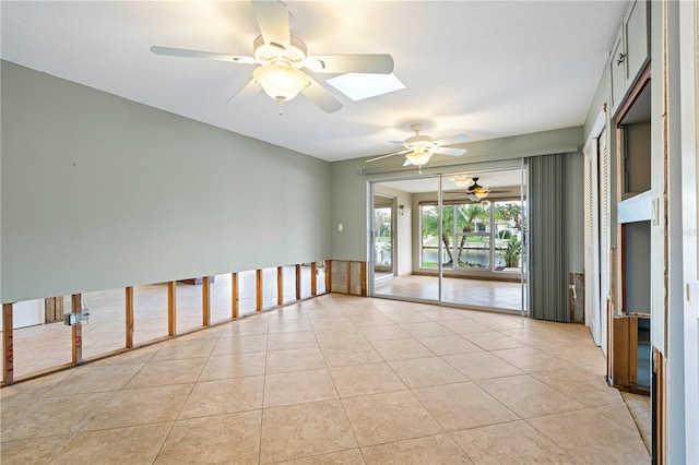 empty room featuring a skylight, ceiling fan, and light tile patterned flooring