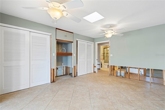 unfurnished bedroom with light tile patterned floors, a skylight, two closets, and ceiling fan