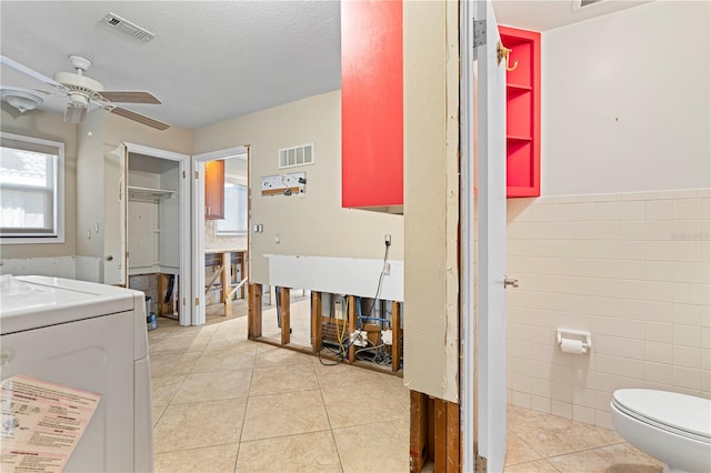 bathroom with tile patterned floors, ceiling fan, toilet, tile walls, and washer / clothes dryer