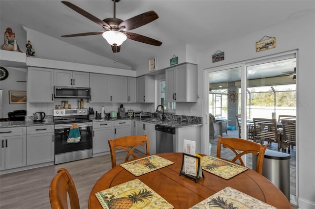 kitchen featuring sink, lofted ceiling, stainless steel appliances, and dark stone counters