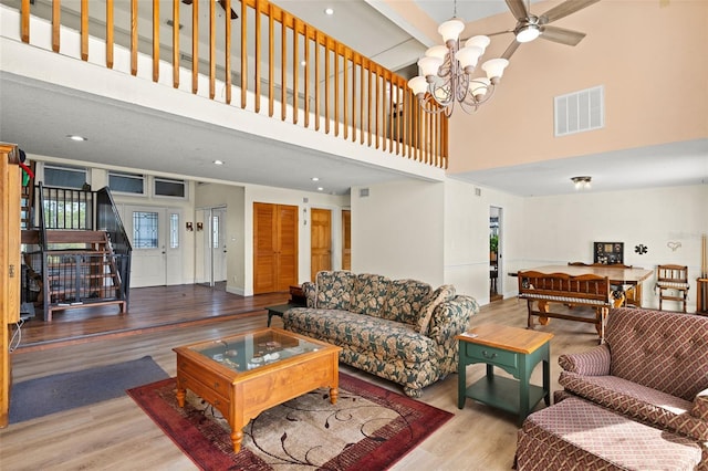 living room with ceiling fan with notable chandelier, wood-type flooring, and a high ceiling