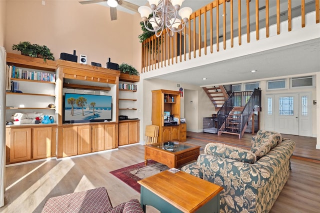 living room with a high ceiling, ceiling fan with notable chandelier, and light hardwood / wood-style floors